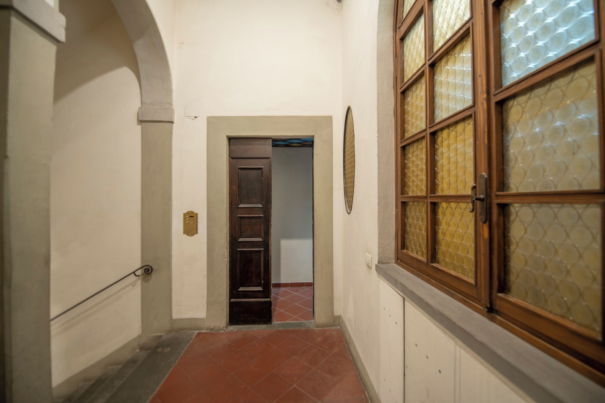 A narrow hallway with a wooden door, a glass door, and a window with a textured pattern.
