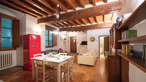 Amplia sala de estar con techo de madera, una mesa de comedor con sillas, un refrigerador rojo, un sofá beige y un mueble de madera con libros.