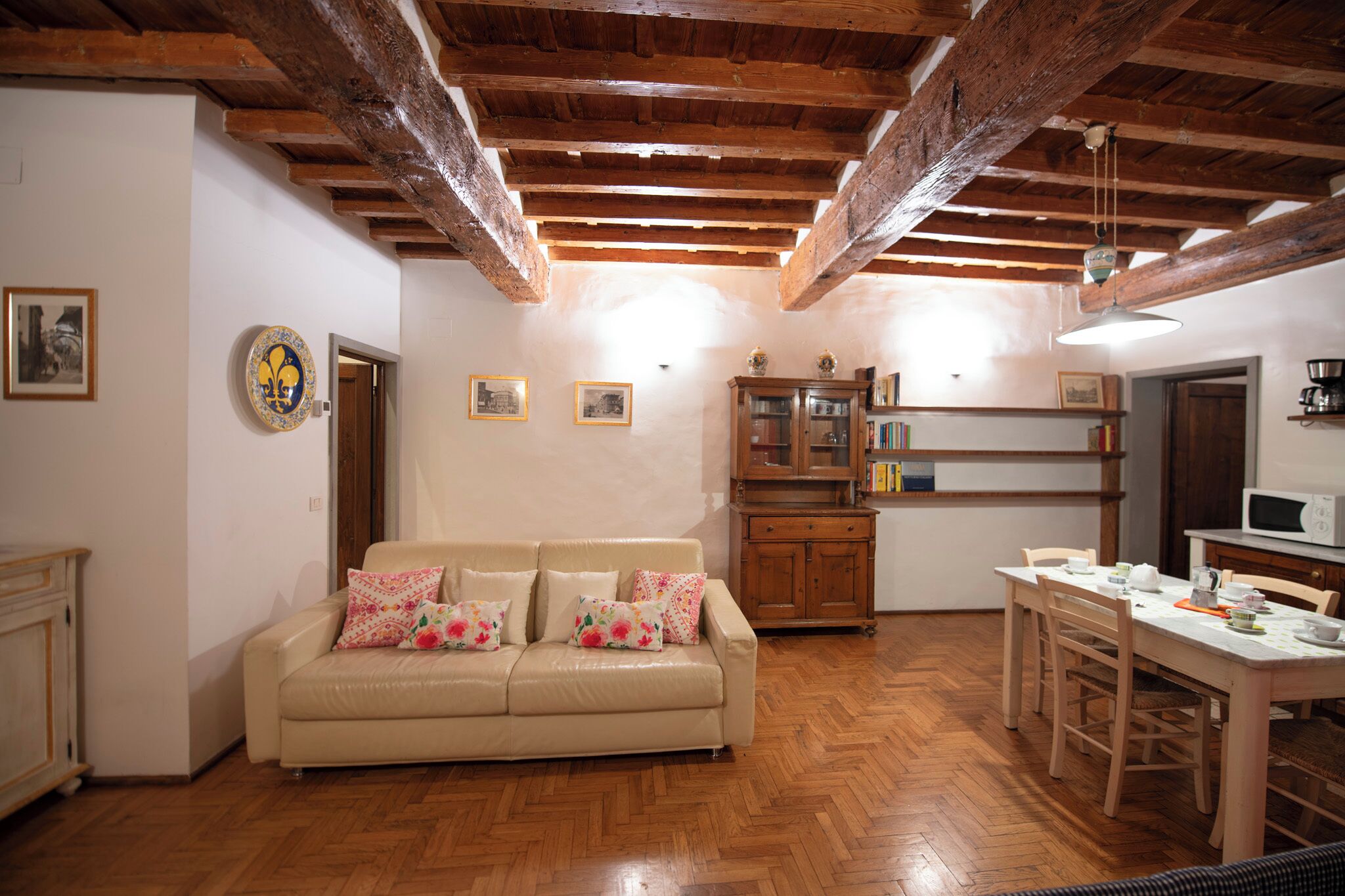 Uma sala de estar acolhedora com teto de madeira, um sofá bege com almofadas florais, um armário de madeira e uma mesa de jantar com cadeiras.