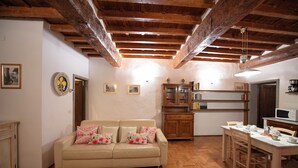 Un salón acogedor con techo de madera, un sofá beige con cojines estampados, un aparador de madera y una mesa de comedor con sillas.