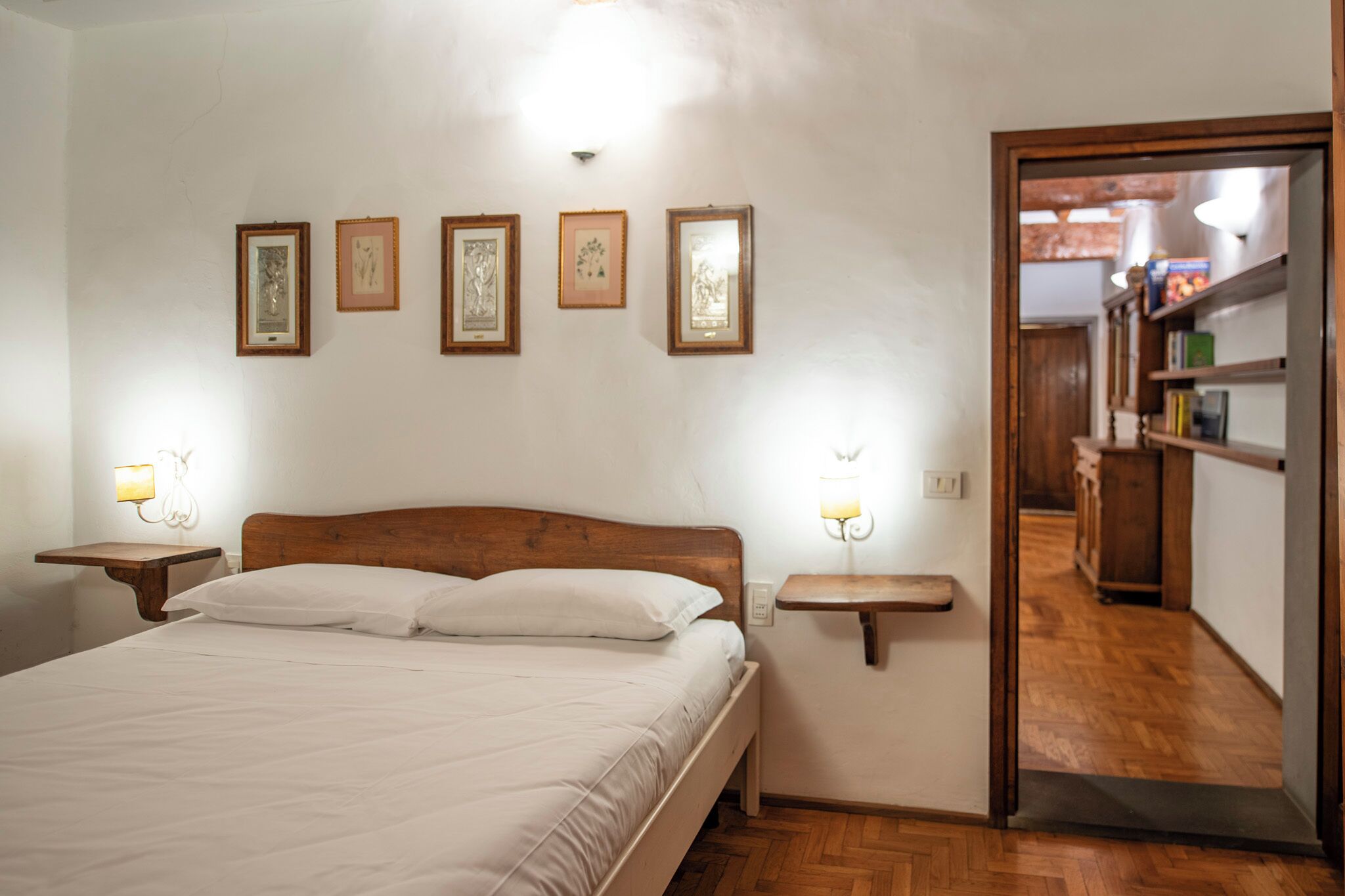 Un dormitorio con una cama de madera, mesitas de noche con lámparas y cuadros en la pared.