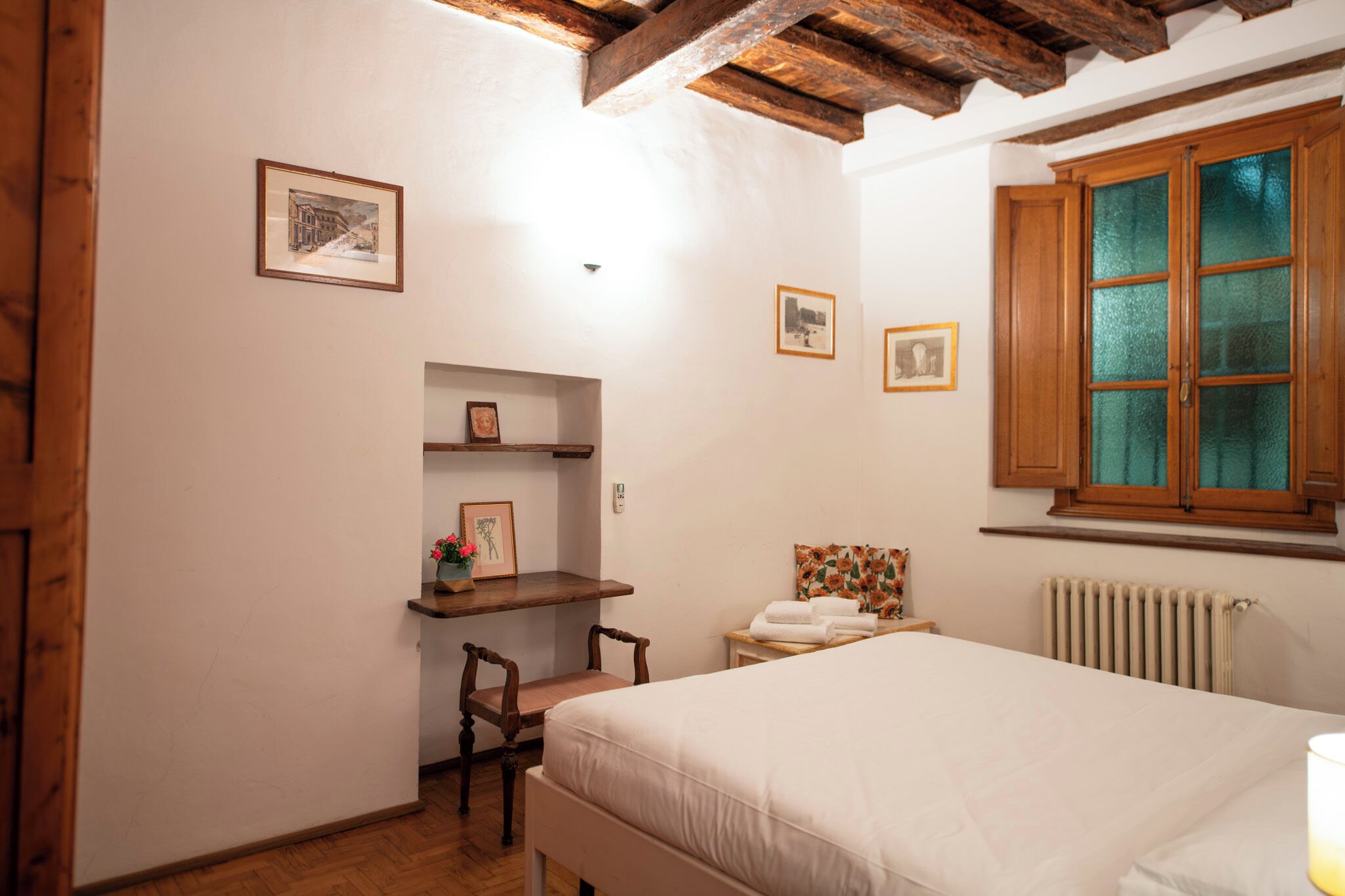 A bedroom with a bed, wooden beams, a radiator, and a window with wooden shutters.