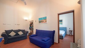 A living room with a blue sofa, a patterned sofa, a bookshelf, and a painting on the wall.