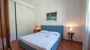 A neatly made bed with white linens, two bedside tables with lamps, a framed picture on the wall, and a sliding door.