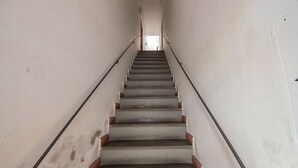 A narrow, straight staircase with a handrail on both sides, leading to a doorway at the top.
