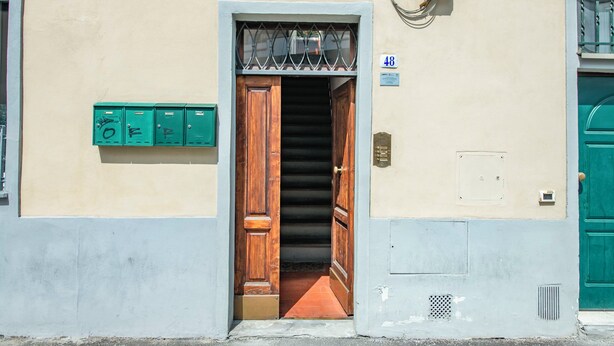 A building entrance with a wooden door, a staircase leading inside, and a green mailbox on the wall.
