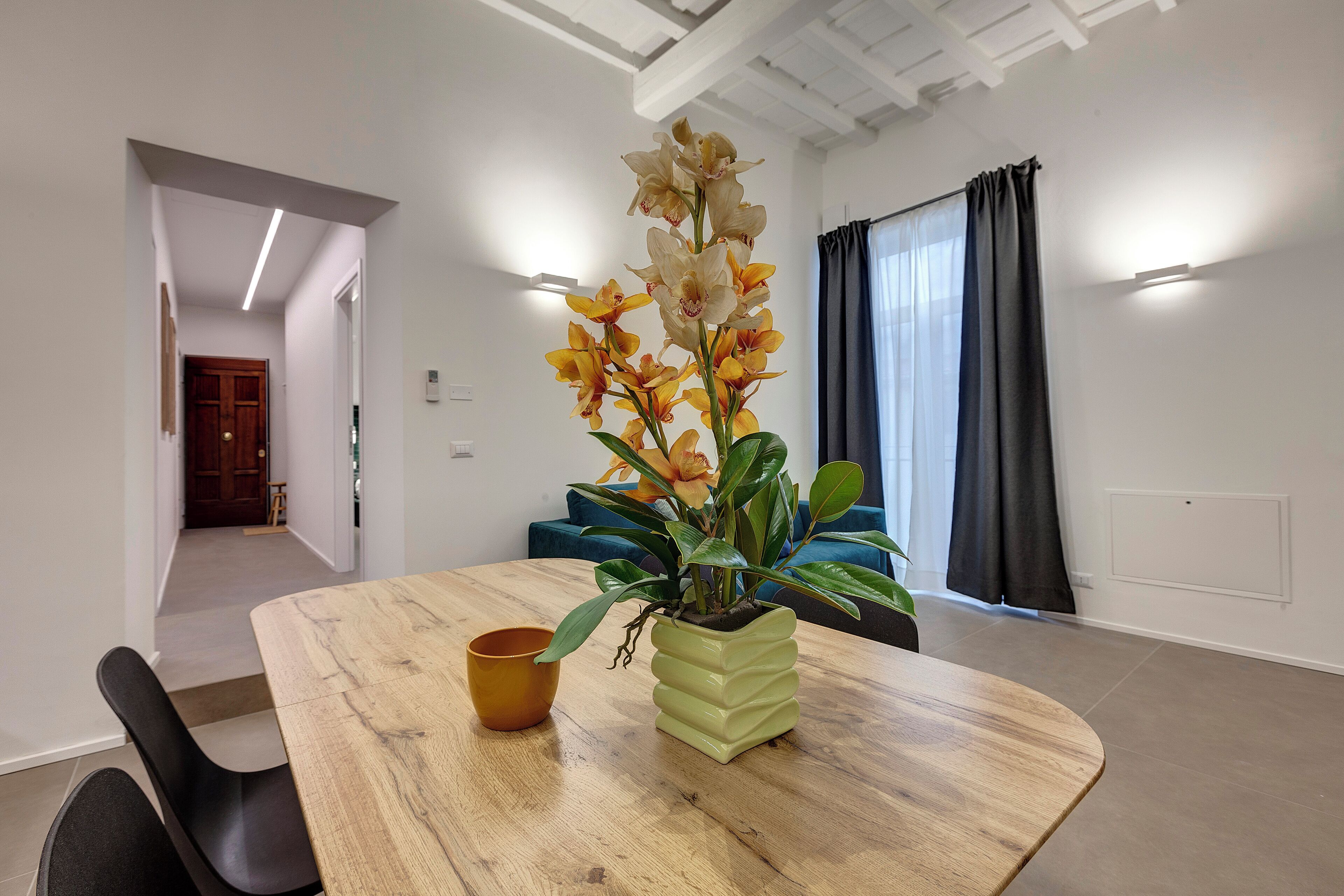 A modern dining area with a wooden table, a potted orchid, and a blue sofa.
