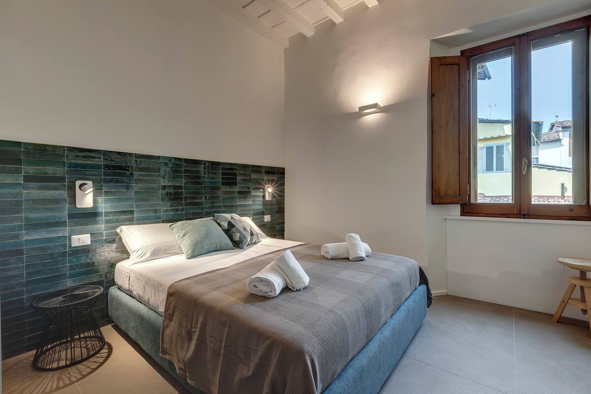 Un dormitorio con cama, mesita de noche, ventana y vistas al exterior.