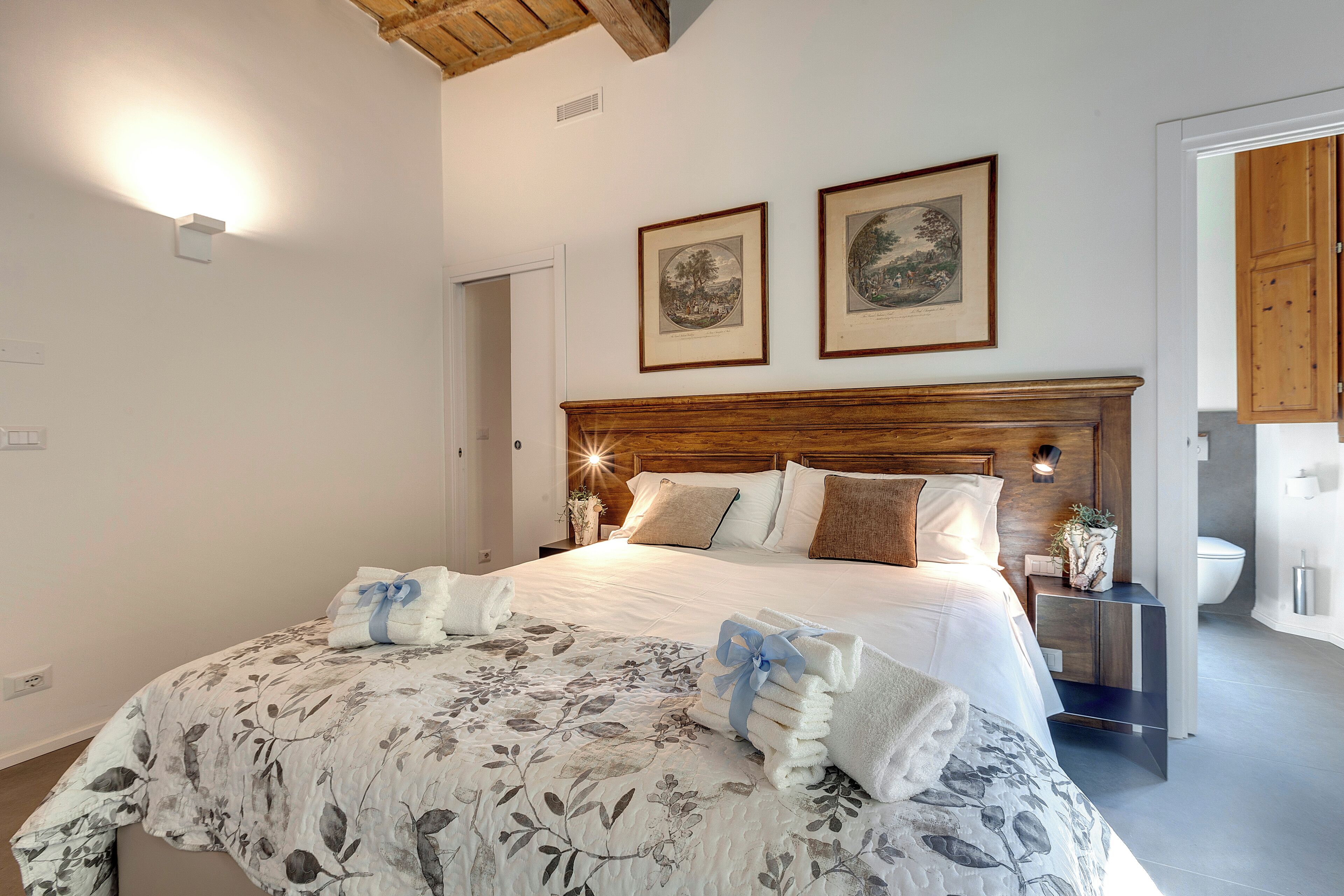 A neatly made bed with floral bedding, a wooden headboard, and two framed pictures on the wall.