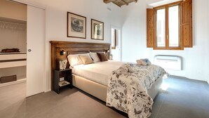 A bedroom with a large bed, wooden headboard, a nightstand, a wardrobe, and a window with wooden shutters. - Mamo Florence - Venere & Zefiro Apartments (Florence)