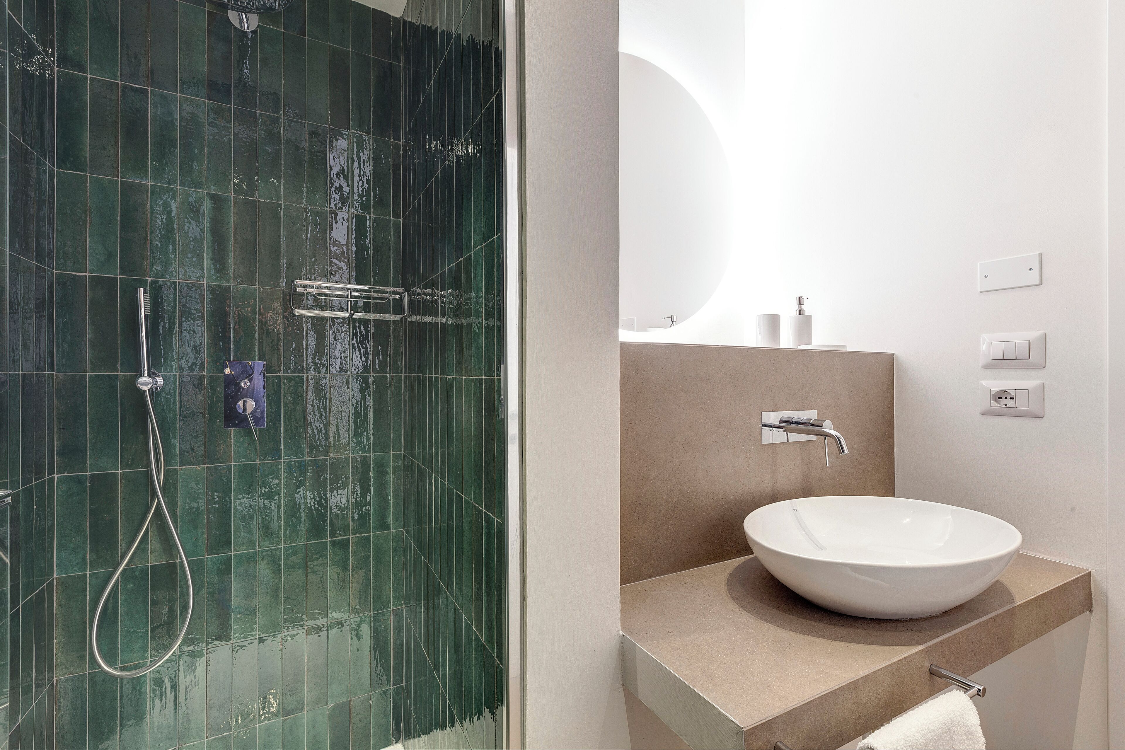 Une salle de bain moderne avec une douche à l’italienne en verre, un lavabo blanc et un plan de toilette beige.
