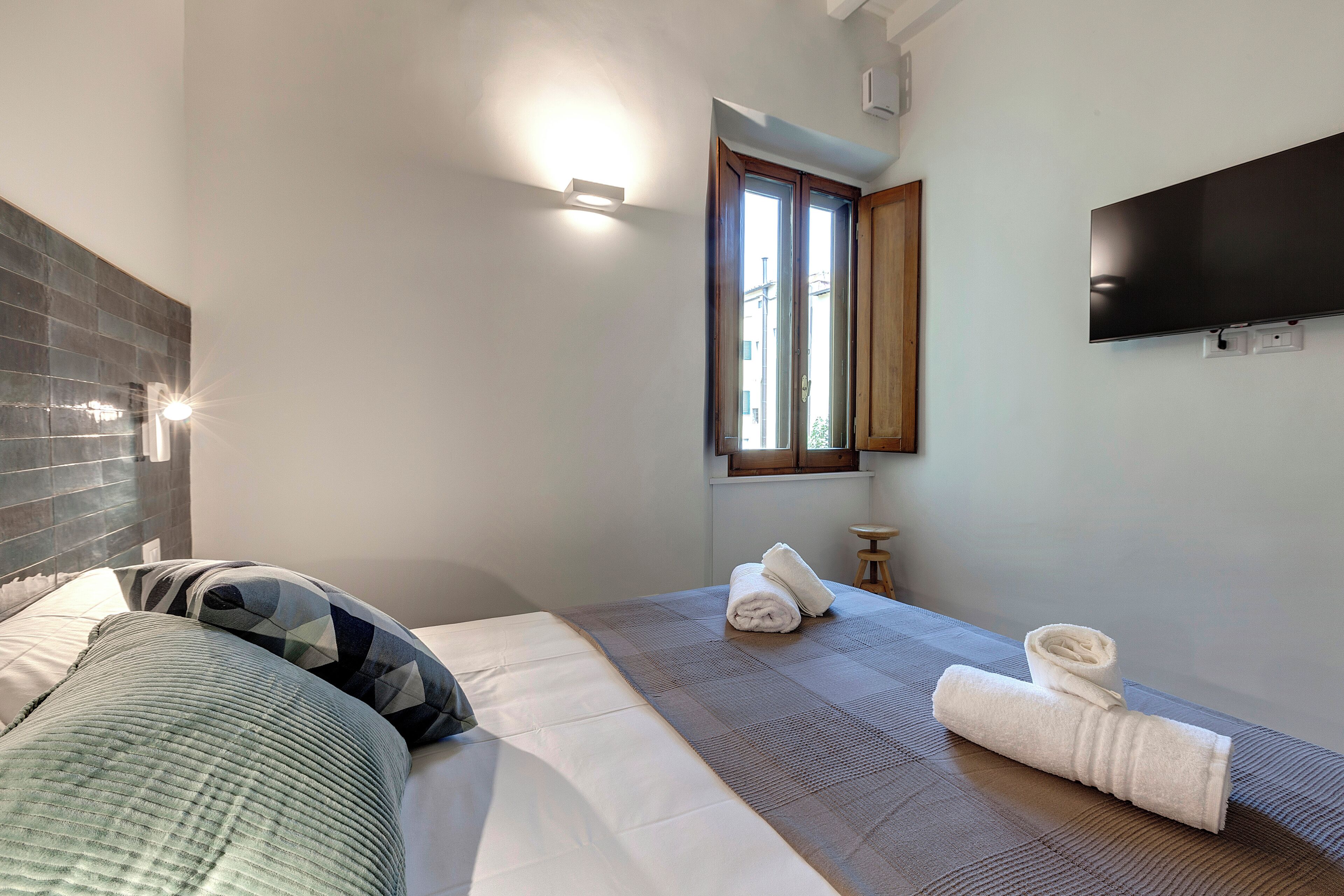 A hotel room with a bed, a window, a flat-screen TV, and a small table.