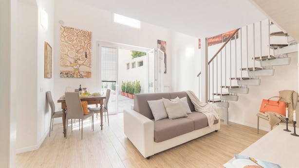 Una sala de estar moderna con sofá, mesa de comedor, sillas y una escalera.