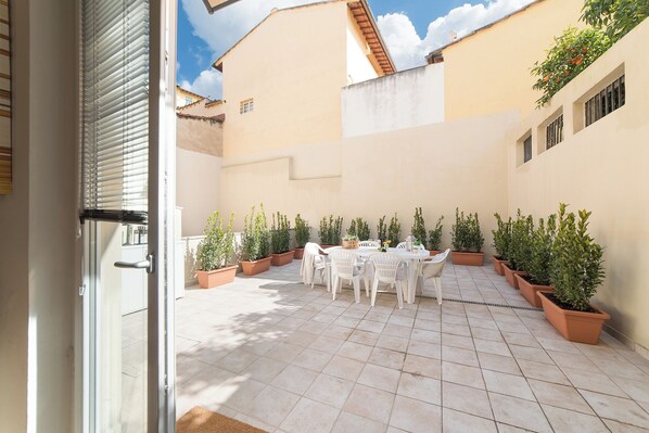 Un patio al aire libre con una mesa y sillas, rodeado de plantas en macetas.