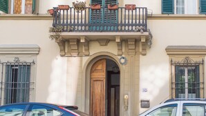 Un edificio con una puerta de madera, un balcón con jardineras y dos coches aparcados delante.