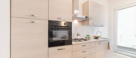 Una cocina moderna con armarios de madera clara, electrodomésticos de acero inoxidable y un amplio ventanal que proporciona luz natural.