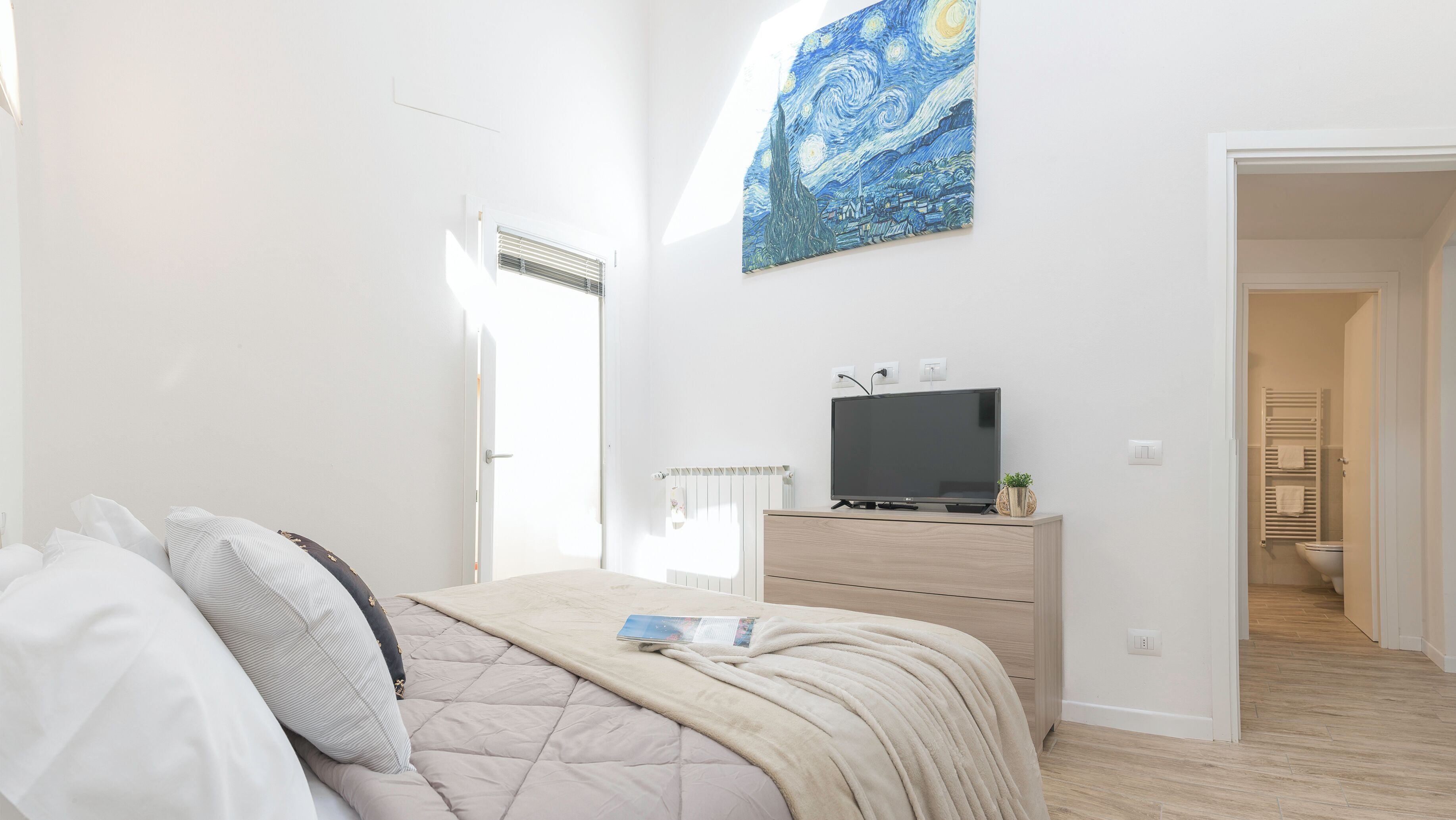 A bedroom with a bed, a dresser, a TV, and a painting on the wall.