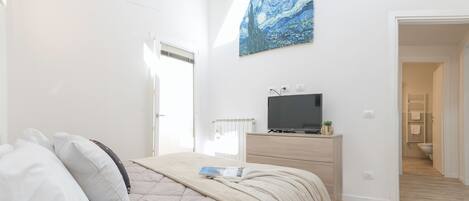 A bedroom with a bed, a dresser, a TV, and a painting on the wall.