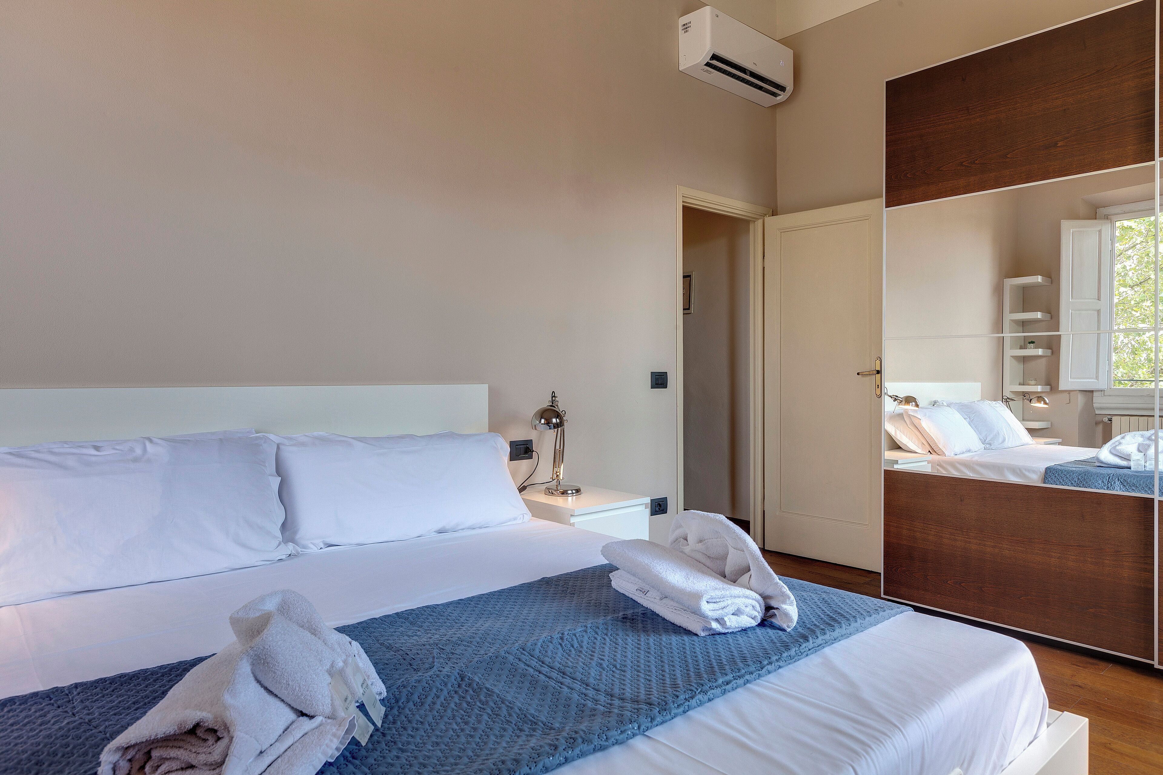 Une chambre d’hôtel avec un grand lit, une lampe de chevet, un miroir et une porte donnant sur une autre pièce.
