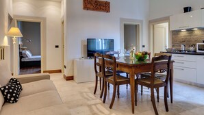 Ein modernes Wohnzimmer mit Esstisch, Holzstühlen, einer Couch, einem Fernseher und einer Küchenzeile mit Schränken und einer Arbeitsplatte.
