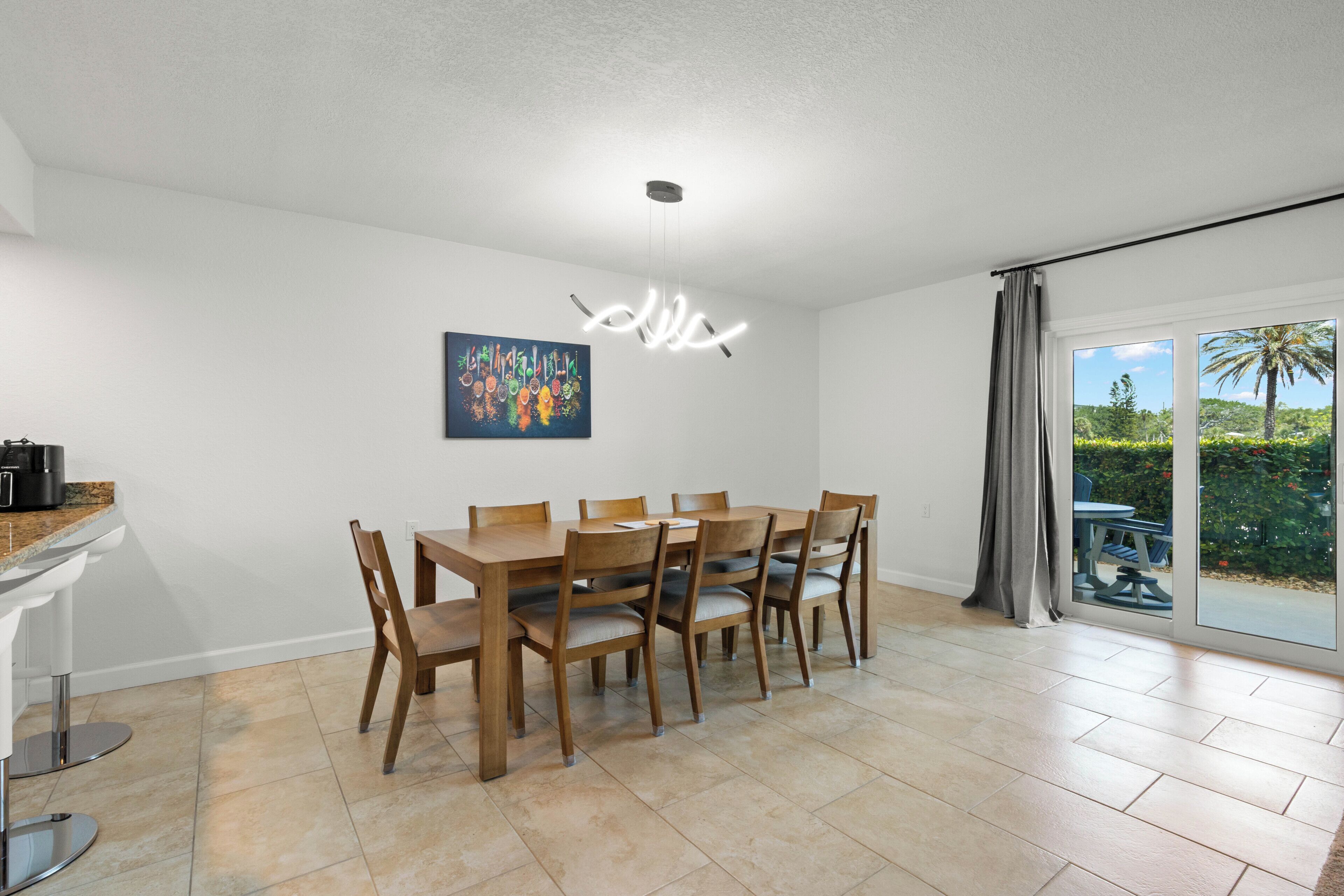Un coin repas avec une table et des chaises, un tableau accroché au mur et une vue à travers une porte vitrée.