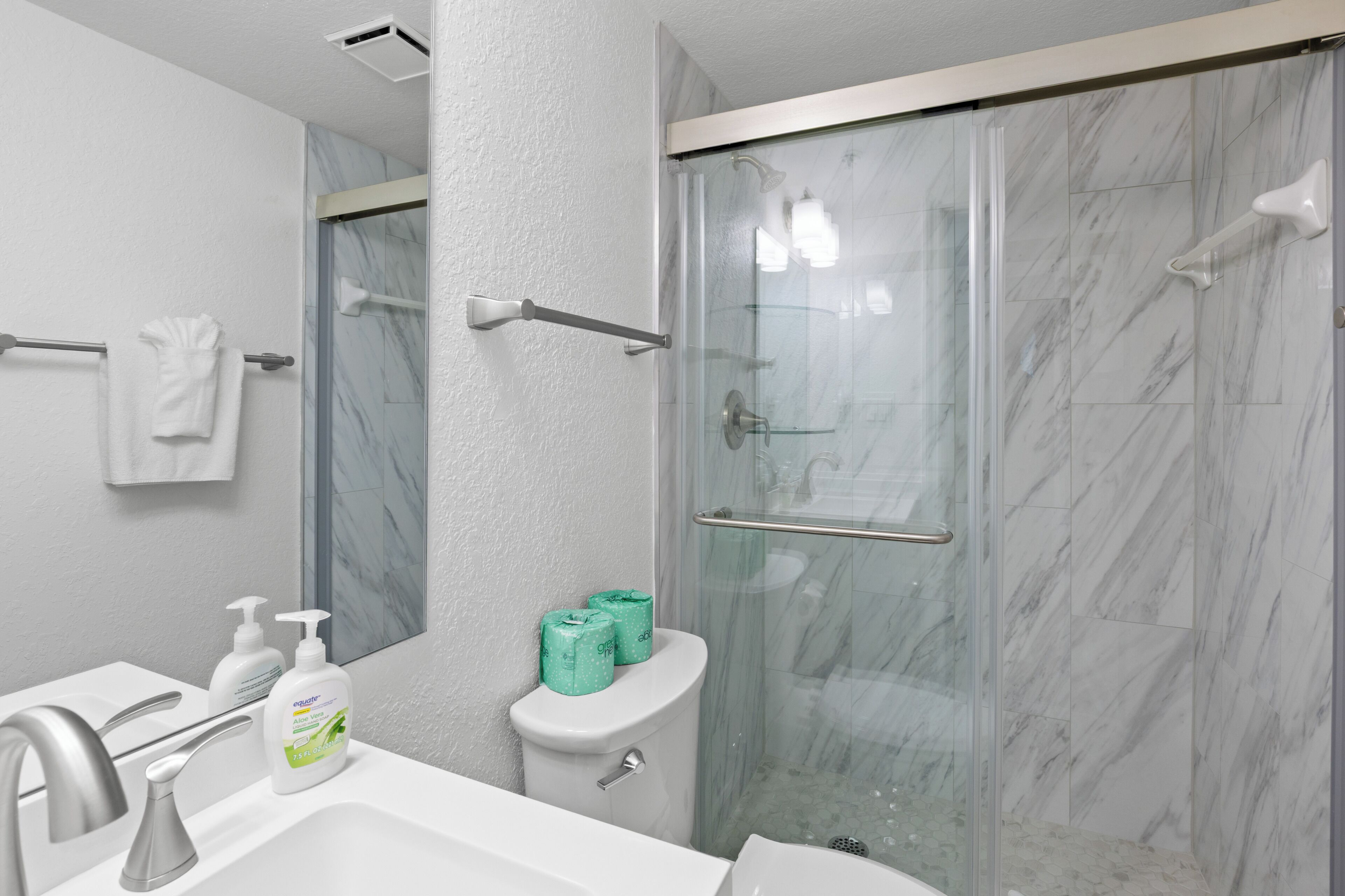 Casa de banho com chuveiro separado por vidro, lavatório branco e sanita.