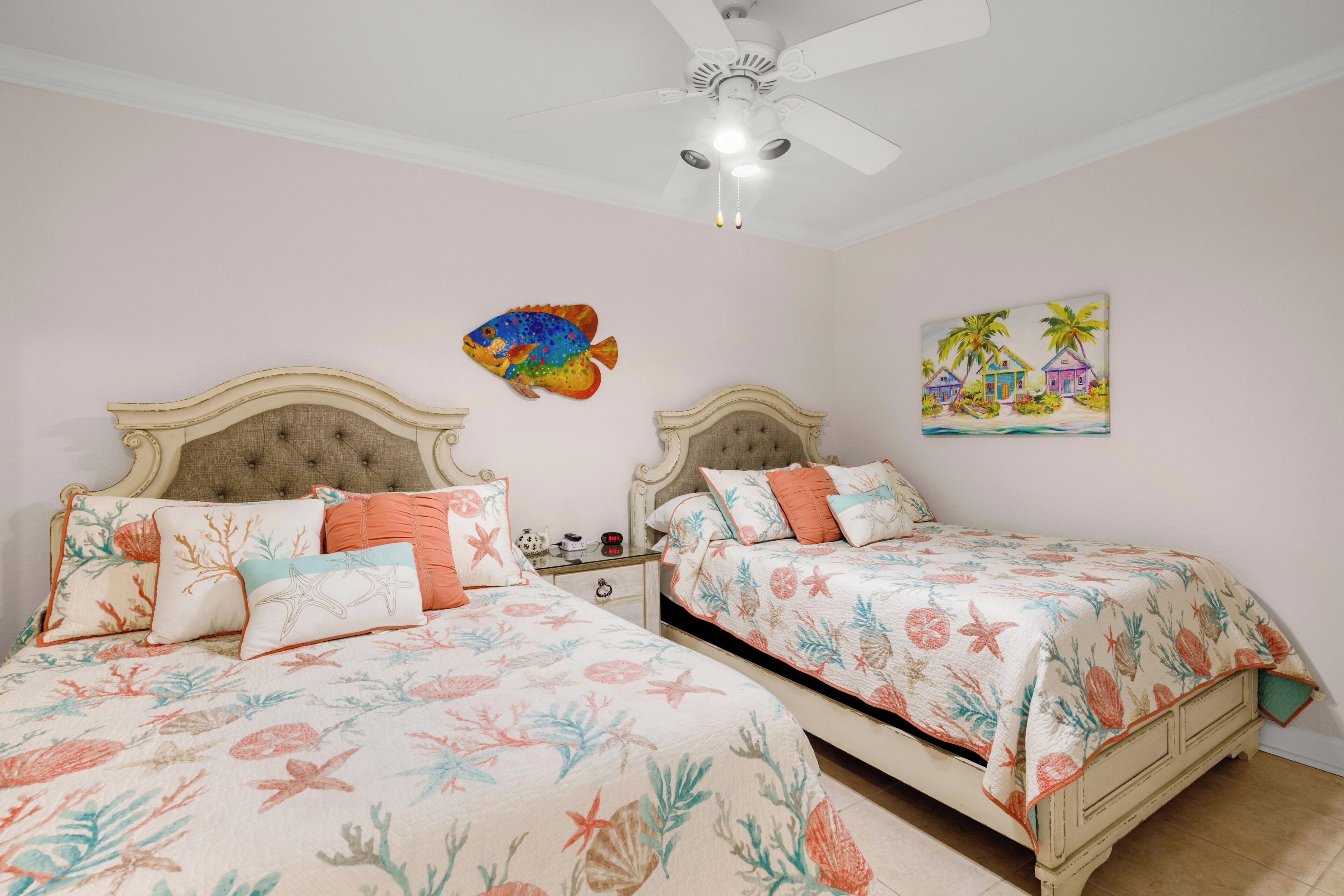 A bedroom with two beds, a ceiling fan, and a wall painting.