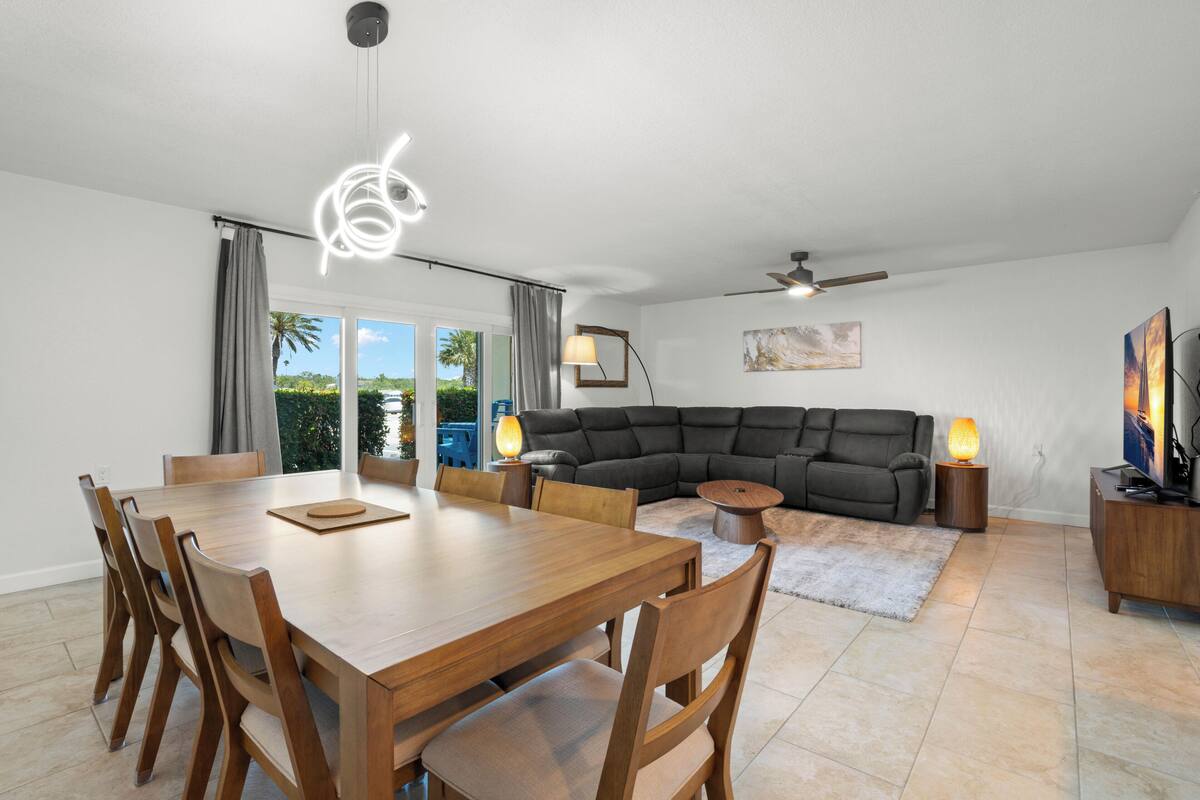 Un coin repas avec une table et des chaises en bois, un canapé, un ventilateur de plafond et un téléviseur posé sur un meuble en bois.