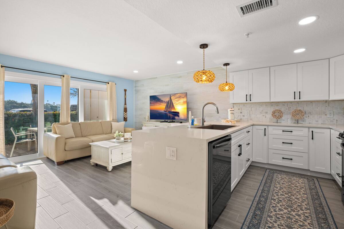 Une cuisine moderne avec des meubles blancs, un îlot central et des luminaires suspendus.