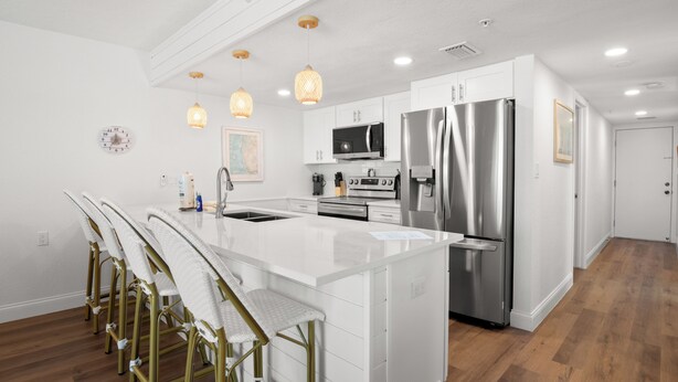 A modern kitchen with white cabinetry, stainless steel appliances, and a central island with bar stools. - Fifty Gulfside Condominiums (Indian Rocks Beach)