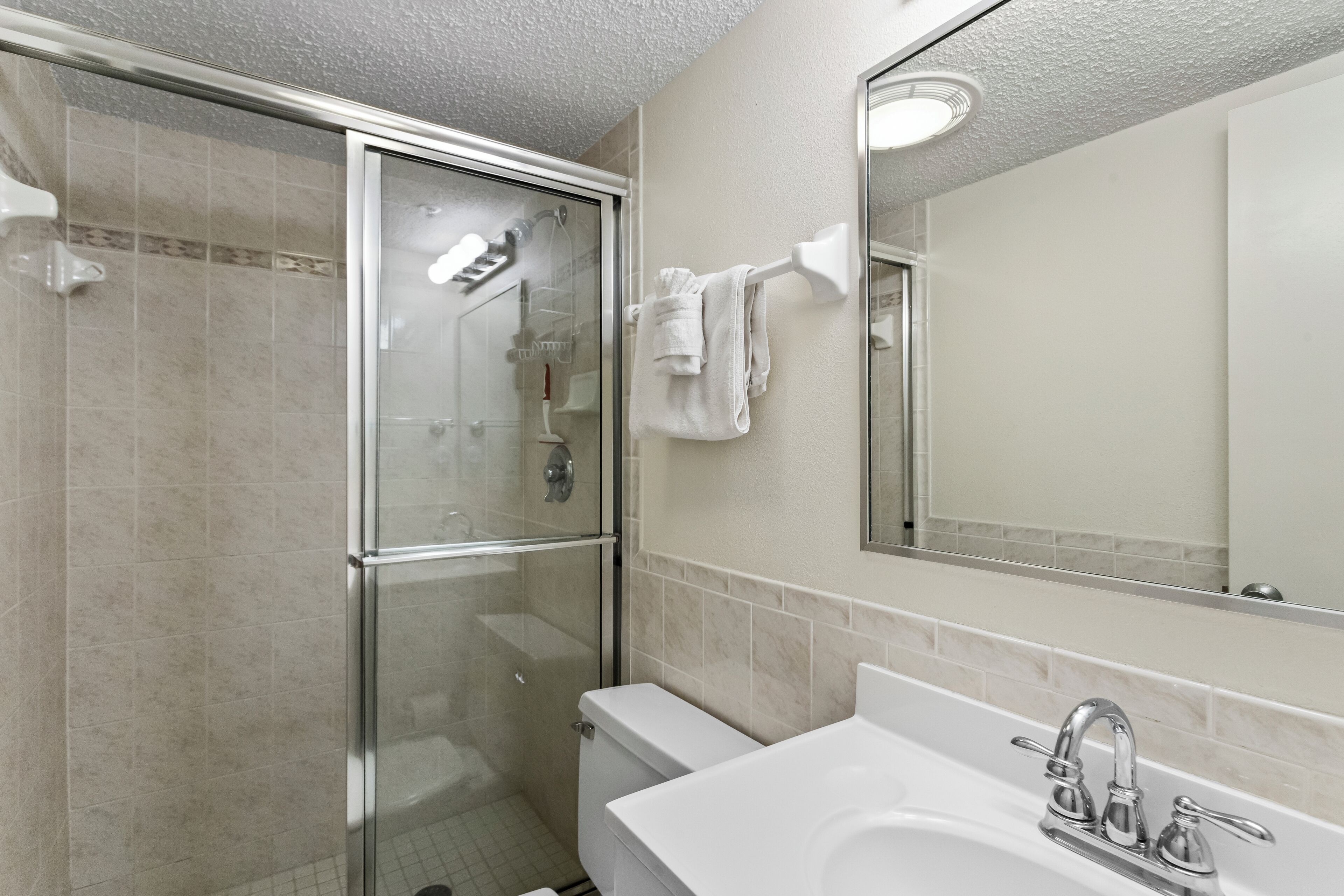 Een moderne badkamer met een douche met glazen wand, een wit wastafelmeubel met een chromen kraan en een spiegel erboven.