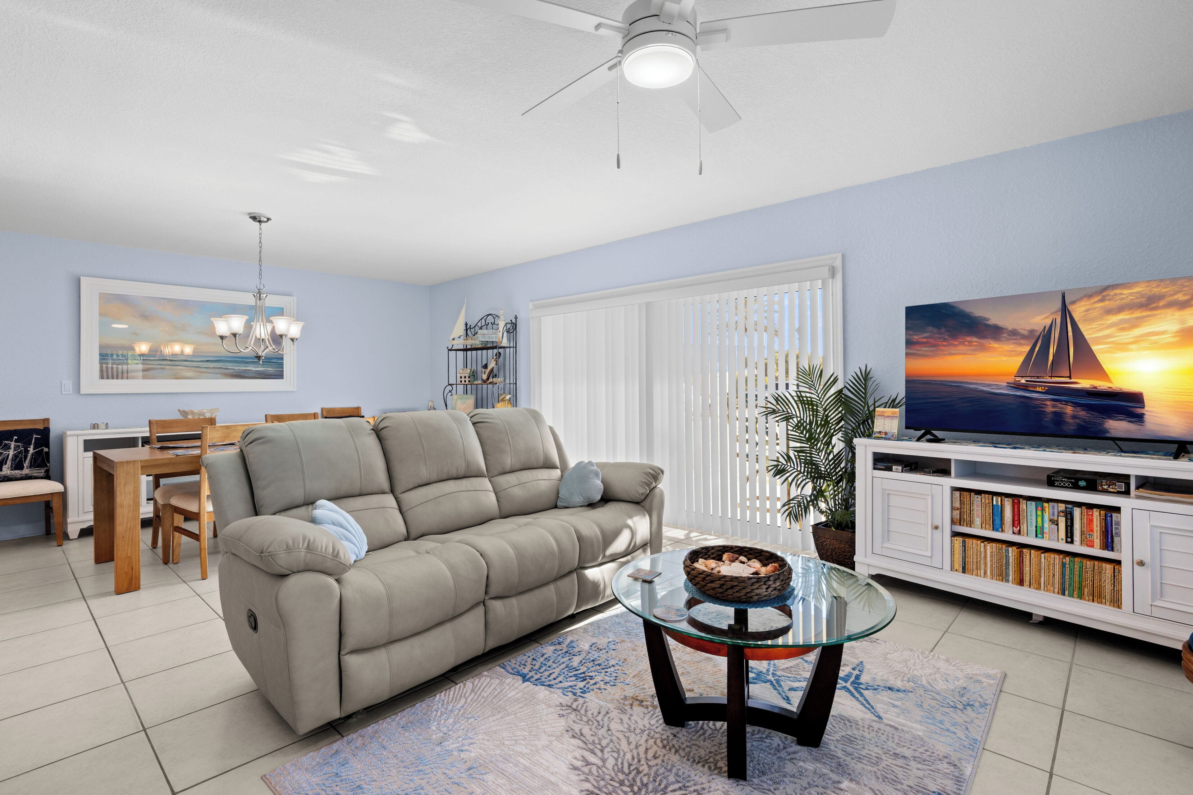 A living room with a sofa, a glass coffee table, a TV, a bookshelf, and a dining area with chairs and a table.