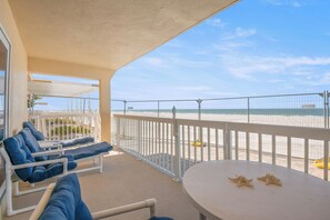 Uma varanda com cadeiras de descanso, uma mesa e vista para a praia.