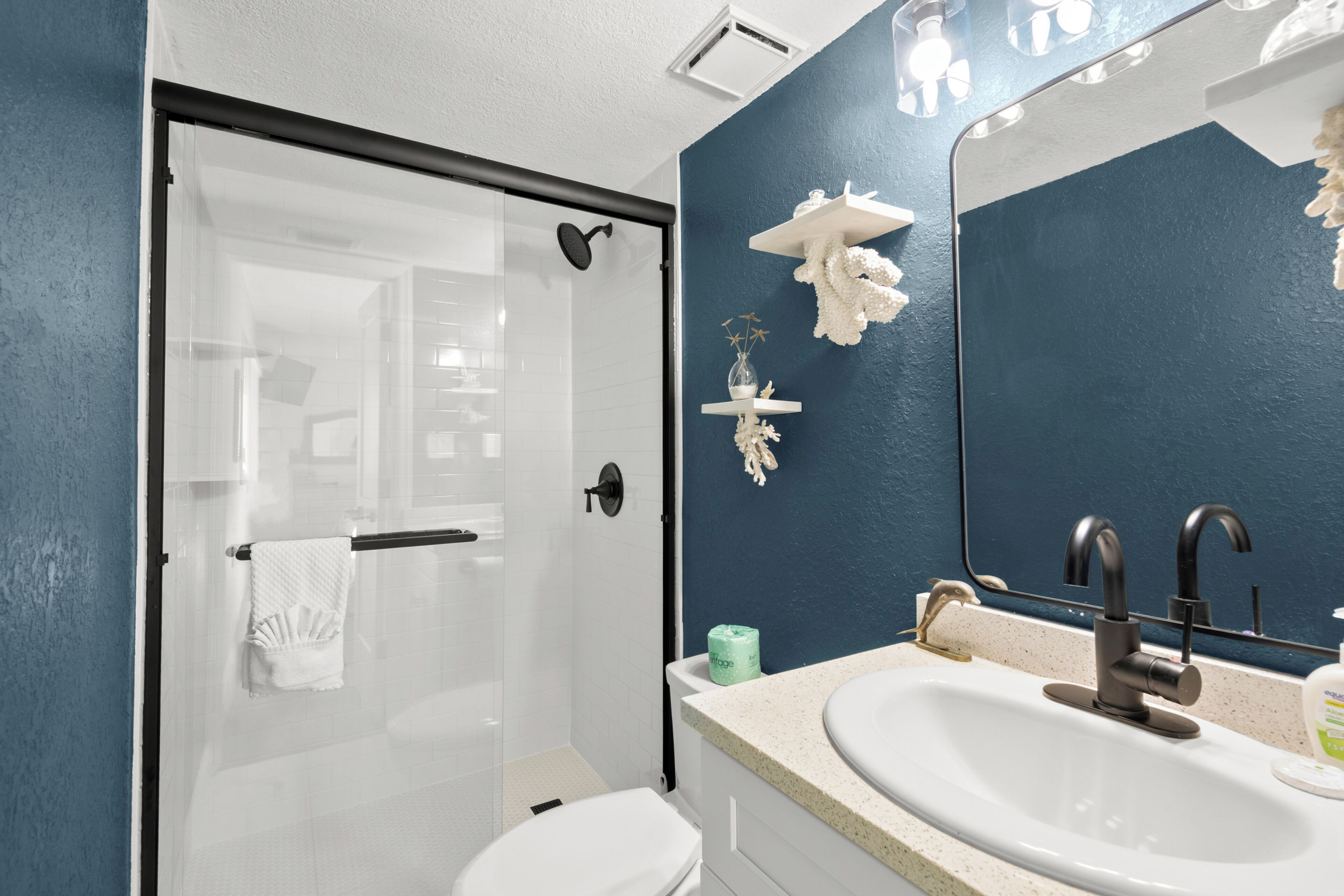 A bathroom with a glass shower door, a white toilet, a sink with a mirror above it, and a blue accent wall.
