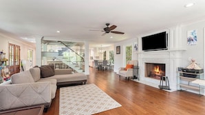 A spacious living room with a fireplace, a television mounted above it, and a staircase leading to an upper level. - Private 4-Bedroom Lakeside Estate Sleeps 10 with Pool, Fire-pit, Wi-Fi, AC (Hollywood)