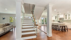 A spacious living area with a wooden staircase, a kitchen with bar stools, and a balcony with a view. - Private 4-Bedroom Lakeside Estate Sleeps 10 with Pool, Fire-pit, Wi-Fi, AC (Hollywood)