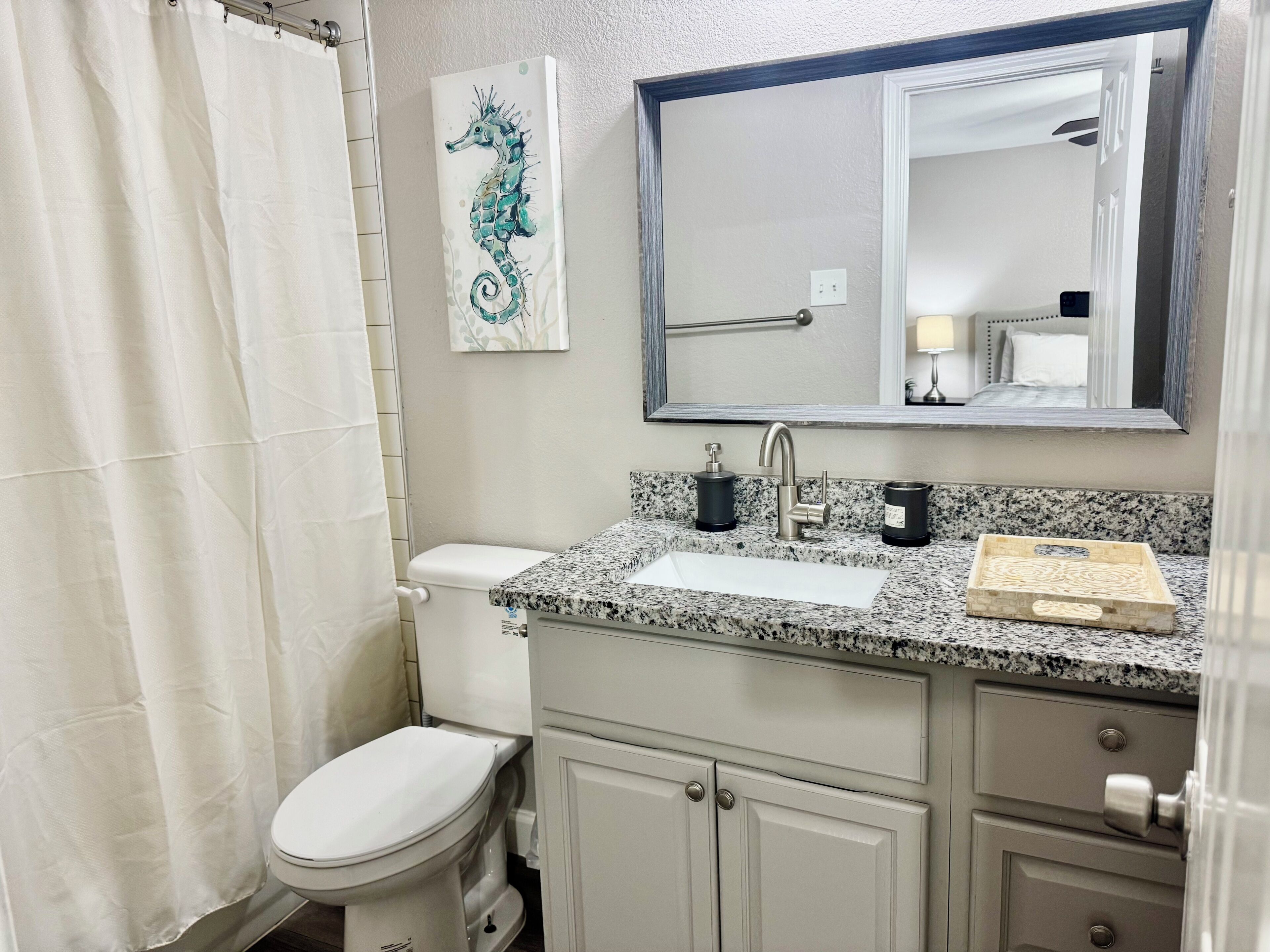 Baño con inodoro, lavamanos, espejo y un cuadro de un caballito de mar.