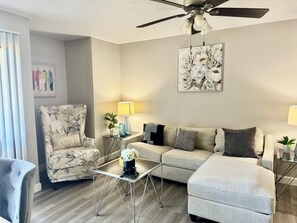 A living room with a sofa, armchair, coffee table, and a ceiling fan.