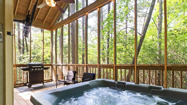 A hot tub on a wooden deck with a view of a forest. - Couples Cabin | Screened Hot Tub, Outdoor TV & King Bed · Near Helen, GA (Sautee Nacoochee)