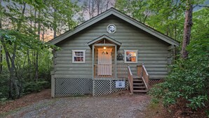 A log cabin with a porch, a door, and a staircase leading up to the entrance. - Couples Cabin | Screened Hot Tub, Outdoor TV & King Bed · Near Helen, GA (Sautee Nacoochee)