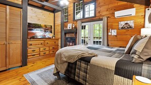 A wooden cabin interior with a bed, dresser, and fireplace. - Couples Cabin | Screened Hot Tub, Outdoor TV & King Bed · Near Helen, GA (Sautee Nacoochee)