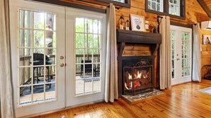 A wooden interior with a fireplace, large windows, and a door leading outside. - Couples Cabin | Screened Hot Tub, Outdoor TV & King Bed · Near Helen, GA (Sautee Nacoochee)
