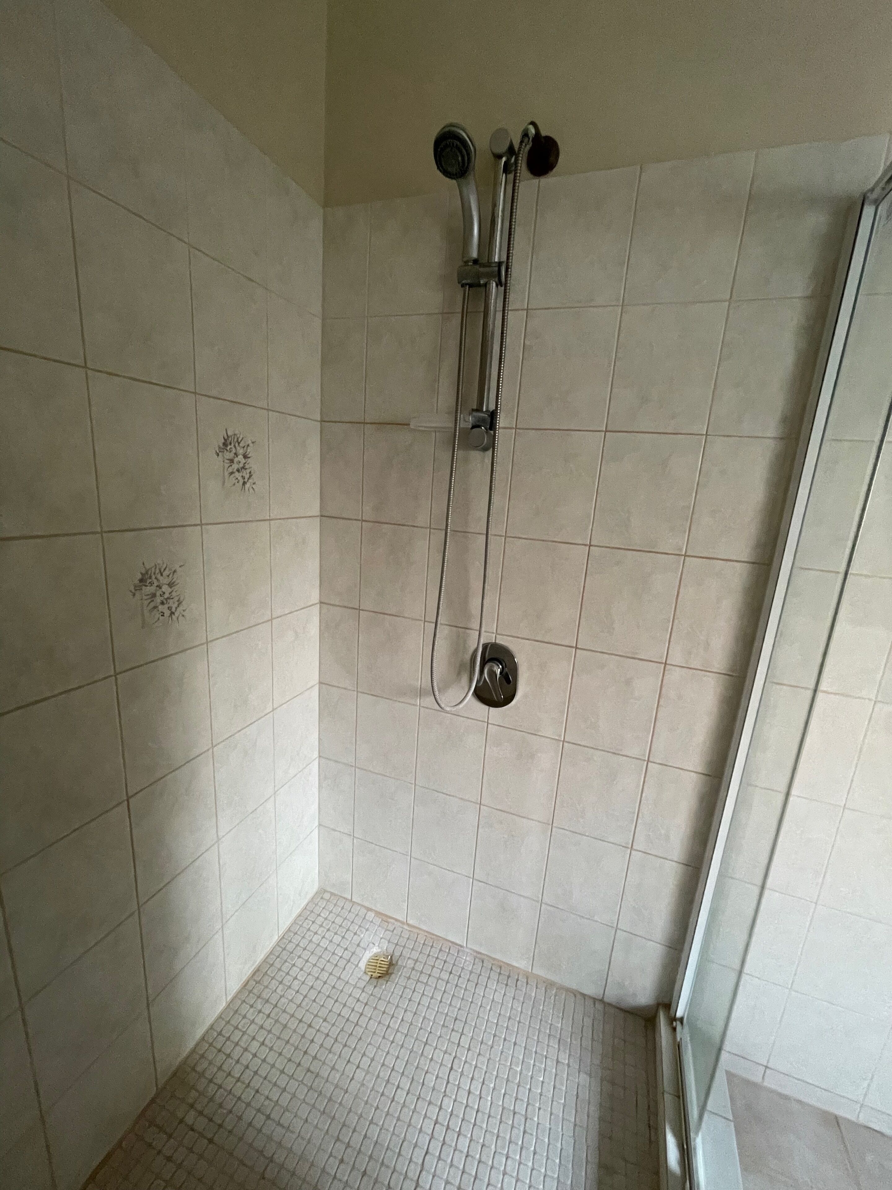 A shower area with tiled walls and floor, a showerhead, and a glass door.