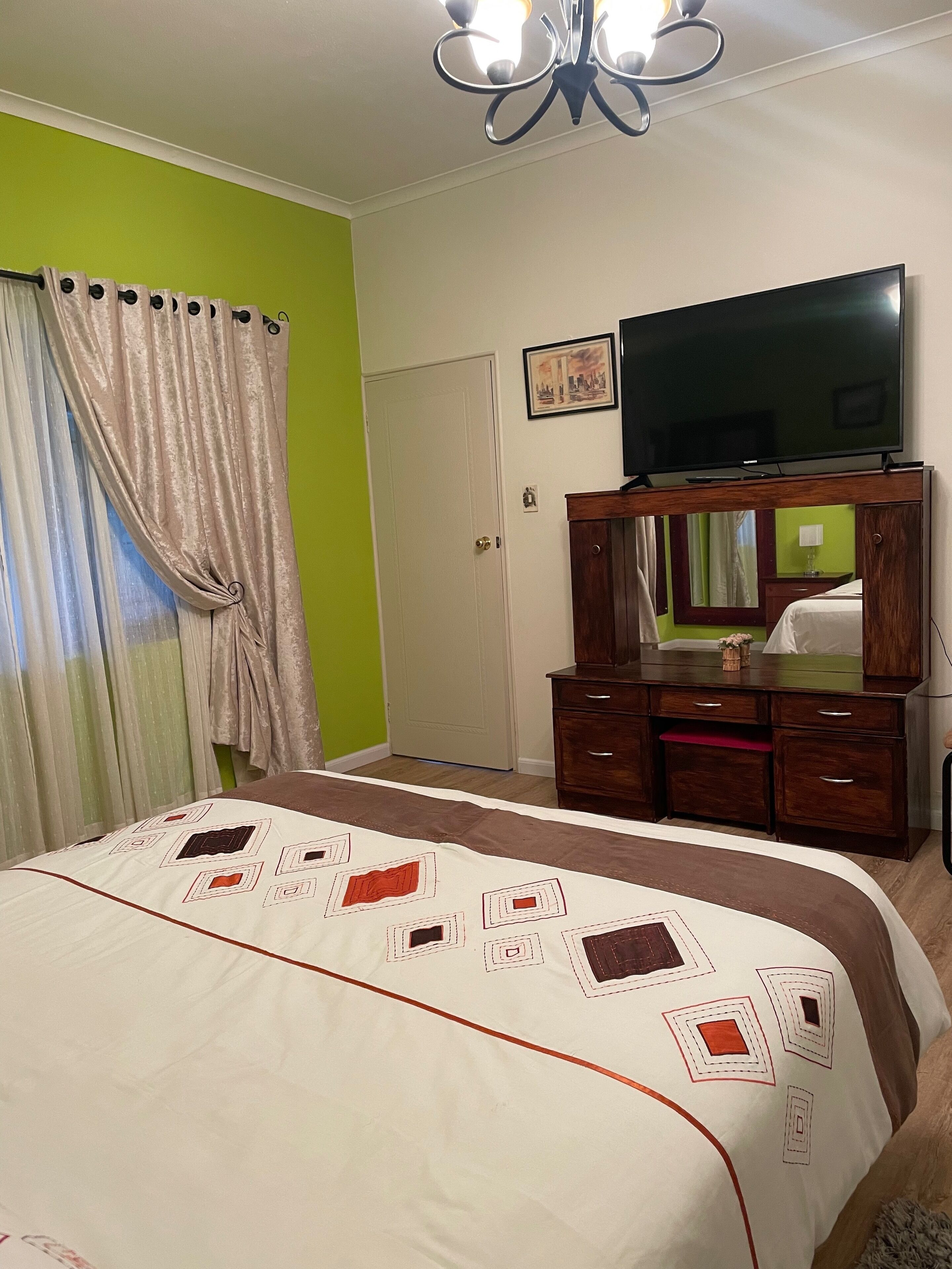 A bedroom with a bed, a dresser, a television, and a door.