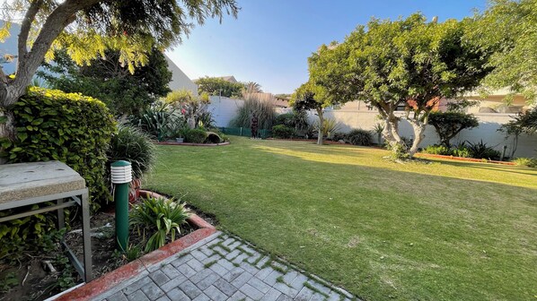 A well-maintained garden with a paved pathway, various plants, and a statue.