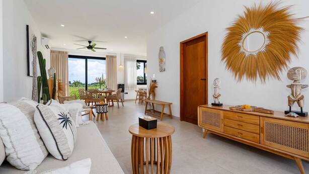 A modern living room with a sofa, round wooden table, and a wooden cabinet with decorative items. - Villa Sawahku (Canggu)