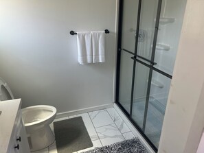 A bathroom with a toilet, a shower with a glass door, a towel rack with a towel, and a marble-patterned floor. - Malbec Cabin @ Vinyard Winery, 3 Adults, 1 Kid, WiFi, AC, Fallbrook (Fallbrook)