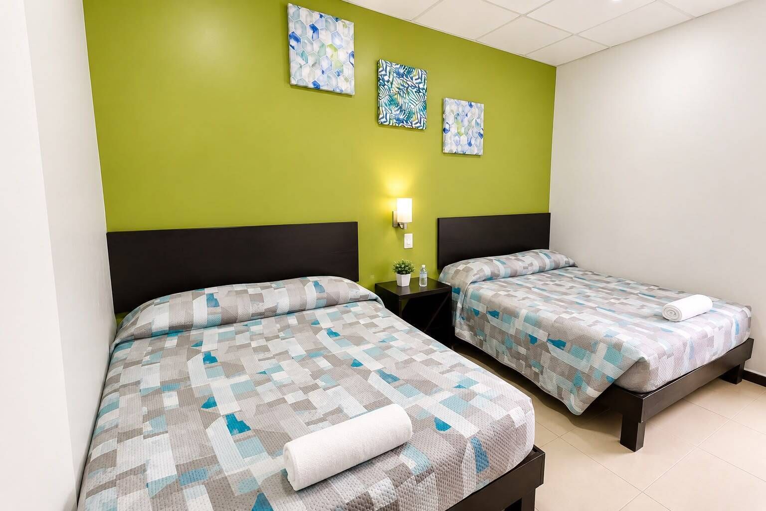 A hotel room with two beds, a green accent wall, and three artworks.