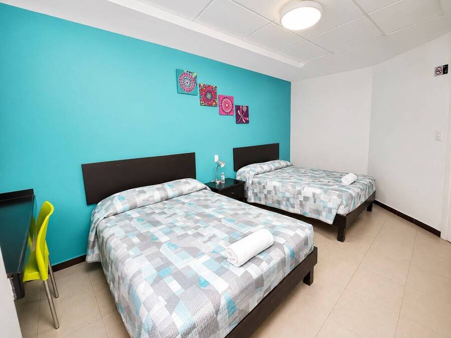 A hotel room with two beds, a desk, a chair, and artwork on the wall.