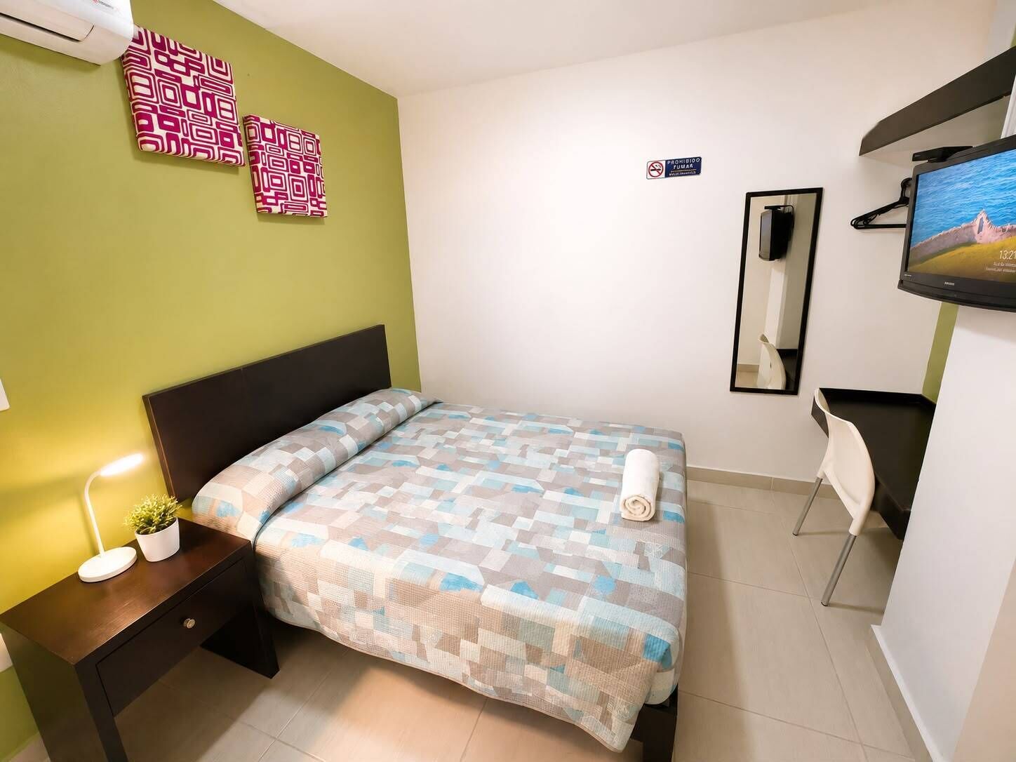Une chambre d’hôtel avec un lit, un bureau avec une lampe, une télévision et un miroir.